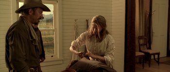 Movie still from “Open Range” (2003), directed by Kevin Costner – A woman sitting on a bed in a room with a window in the background; Medium shot, Over the shoulder angle
