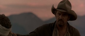 Movie still from “Open Range” (2003), directed by Kevin Costner – A man wearing a cowboy hat in front of mountains; Close Up shot, Over the shoulder angle