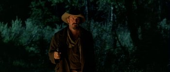 Movie still from “Open Range” (2003), directed by Kevin Costner – A man in a cowboy hat holding a gun in the dark; Medium shot, Low angle