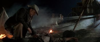 Movie still from “Open Range” (2003), directed by Kevin Costner – A man in a cowboy hat is sitting next to a fire; Medium shot, Low angle