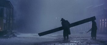 Movie still from “Open Range” (2003), directed by Kevin Costner – A man carrying a large piece of wood in the rain; Wide shot, Low angle