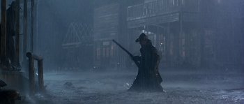 Movie still from “Open Range” (2003), directed by Kevin Costner – A man holding a sword in the middle of a street; Wide shot, Low angle