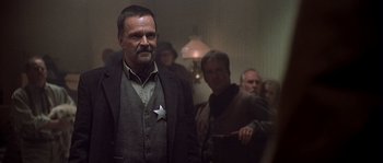 Movie still from “Open Range” (2003), directed by Kevin Costner – A group of people standing in a room; Medium shot, Low angle