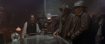 Movie still from “Open Range” (2003), directed by Kevin Costner – A group of men standing next to a table; Medium shot, Low angle