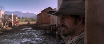 Movie still from “Open Range” (2003), directed by Kevin Costner – A man wearing a cowboy hat standing next to horses; Close Up shot, Low angle