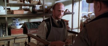 Movie still from “Open Range” (2003), directed by Kevin Costner – A man with a beard wearing an apron and a tie; Medium shot, Over the shoulder angle