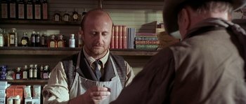 Movie still from “Open Range” (2003), directed by Kevin Costner – A man wearing an apron is holding a cell phone in his hand; Medium shot, Over the shoulder angle