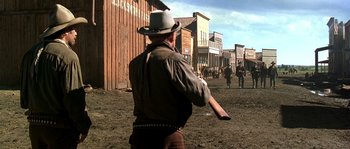 Movie still from “Open Range” (2003), directed by Kevin Costner – A man in a cowboy hat is holding a frisbee; Wide shot, Low angle