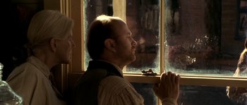 Movie still from “Open Range” (2003), directed by Kevin Costner – A man standing in front of a window with his hands clasped together; Close Up shot, Over the shoulder angle