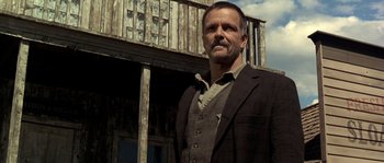 Movie still from “Open Range” (2003), directed by Kevin Costner – A man standing in front of an old wooden building; Medium shot, Low angle