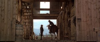 Movie still from “Open Range” (2003), directed by Kevin Costner – A man on a horse talking to another man in a barn; Wide shot, Over the shoulder angle