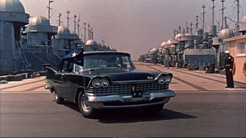 Movie still from “Operation Petticoat” (1959), directed by Blake Edwards – An old car driving down a street past a row of buildings; Wide shot, Low angle