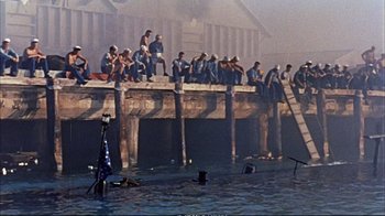 Movie still from “Operation Petticoat” (1959), directed by Blake Edwards – A group of people sitting on top of a wooden dock; Extreme Wide shot, High angle