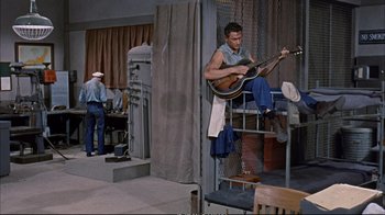 Movie still from “Operation Petticoat” (1959), directed by Blake Edwards – A man playing a guitar while another man watches; Wide shot, High angle