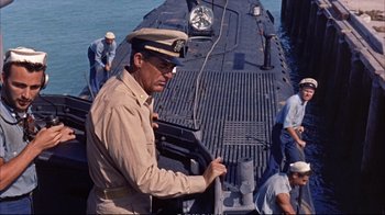 Movie still from “Operation Petticoat” (1959), directed by Blake Edwards – A man in a hat is standing on a boat; Medium shot, High angle