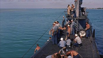 Movie still from “Operation Petticoat” (1959), directed by Blake Edwards – A group of men standing on a pier near the ocean; Extreme Wide shot, High angle
