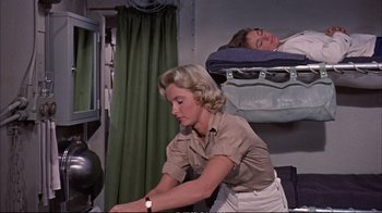 Movie still from “Operation Petticoat” (1959), directed by Blake Edwards – A woman sitting on top of a bed next to a man sleeping; Medium shot, Low angle