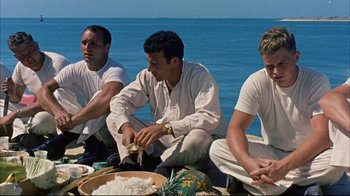 Movie still from “Operation Petticoat” (1959), directed by Blake Edwards – A group of men sitting on the beach preparing food; Medium shot, High angle