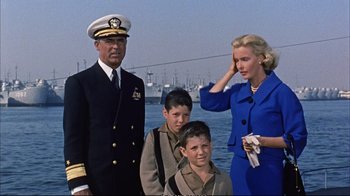 Movie still from “Operation Petticoat” (1959), directed by Blake Edwards – An older man and two young boys and an older woman standing in front of a body of water; Medium shot, Low angle