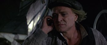 Movie still from “Orca” (1977), directed by Michael Anderson – A man in a hat is talking on a cell phone; Close Up shot, High angle