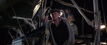 Movie still from “Orca” (1977), directed by Michael Anderson – A man in a hat and sweater holding onto a rope; Medium shot, Low angle
