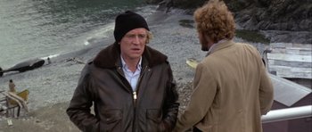 Movie still from “Orca” (1977), directed by Michael Anderson – Two men standing next to each other on a beach; Medium shot, Over the shoulder angle