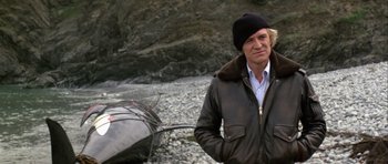 Movie still from “Orca” (1977), directed by Michael Anderson – A man standing next to a boat on a beach; Medium shot, Low angle