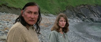 Movie still from “Orca” (1977), directed by Michael Anderson – A man and a woman standing next to each other on a beach; Close Up shot, Low angle