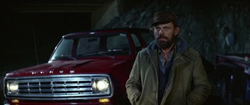 Movie still from “Orca” (1977), directed by Michael Anderson – A man standing in front of a red truck; Medium shot, Over the shoulder angle