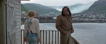 Movie still from “Orca” (1977), directed by Michael Anderson – A man standing next to a woman near a body of water; Medium shot, Over the shoulder angle