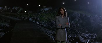 Movie still from “Orca” (1977), directed by Michael Anderson – A woman standing in front of some rocks at night with her arms crossed; Wide shot, Low angle