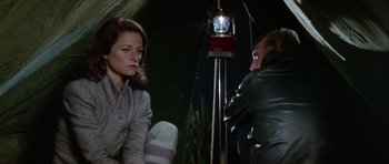 Movie still from “Orca” (1977), directed by Michael Anderson – A man and a woman sitting next to each other in front of a light; Medium shot, Over the shoulder angle