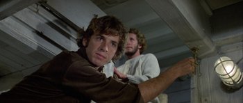 Movie still from “Orca” (1977), directed by Michael Anderson – Two young men standing next to each other in a room; Close Up shot, Low angle
