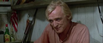 Movie still from “Orca” (1977), directed by Michael Anderson – A man with blonde hair and a pink shirt is smiling; Close Up shot, Over the shoulder angle