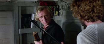 Movie still from “Orca” (1977), directed by Michael Anderson – A man holding a microphone in a room; Close Up shot, Over the shoulder angle