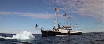 Movie still from “Orca” (1977), directed by Michael Anderson – A boat is sailing in the ocean with a person on the deck; Extreme Wide shot, Low angle