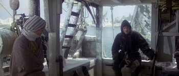 Movie still from “Orca” (1977), directed by Michael Anderson – A man sitting on the deck of a boat in the water; Wide shot, Low angle