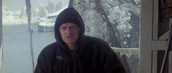 Movie still from “Orca” (1977), directed by Michael Anderson – A man wearing a black hooded jacket sitting in the snow; Medium shot, Low angle