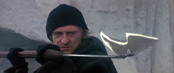 Movie still from “Orca” (1977), directed by Michael Anderson – A man in a black jacket and a black hat holding an axe; Close Up shot, Low angle