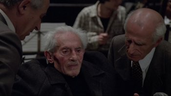 Movie still from “Orchestra Rehearsal” (1978), directed by Federico Fellini – An old man with a white beard is sitting next to two older men; Medium shot, Over the shoulder angle