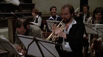Movie still from “Orchestra Rehearsal” (1978), directed by Federico Fellini – A man playing a trumpet in front of a group of people; Medium shot, Over the shoulder angle