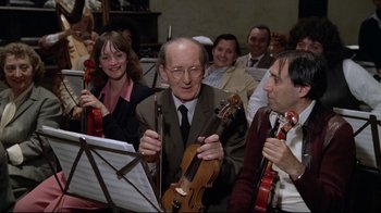 Movie still from “Orchestra Rehearsal” (1978), directed by Federico Fellini – An older man is holding a violin while a group of people are listening; Medium shot, High angle