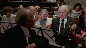 Movie still from “Orchestra Rehearsal” (1978), directed by Federico Fellini – An older man is playing the piano in front of a group of older people; Medium shot, Over the shoulder angle