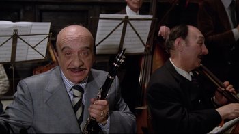 Movie still from “Orchestra Rehearsal” (1978), directed by Federico Fellini – An older man in a suit holding a guitar in front of other men; Close Up shot, Low angle
