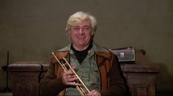 Movie still from “Orchestra Rehearsal” (1978), directed by Federico Fellini – A man holding a trumpet and smiling for the camera; Close Up shot, High angle