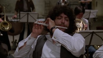 Movie still from “Orchestra Rehearsal” (1978), directed by Federico Fellini – A man playing a flute in front of a crowd; Close Up shot, Low angle