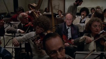 Movie still from “Orchestra Rehearsal” (1978), directed by Federico Fellini – A group of people sitting in a room playing musical instruments; Medium shot, Low angle