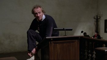 Movie still from “Orchestra Rehearsal” (1978), directed by Federico Fellini – A man sitting at a podium in front of microphones; Medium shot, Low angle