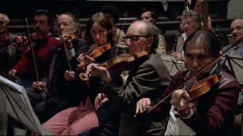 Movie still from “Orchestra Rehearsal” (1978), directed by Federico Fellini – A group of people sitting in a room playing musical instruments; Wide shot, High angle