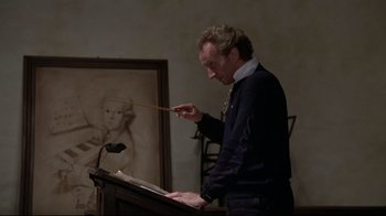 Movie still from “Orchestra Rehearsal” (1978), directed by Federico Fellini – A man standing in front of a podium with a microphone; Medium shot, Low angle